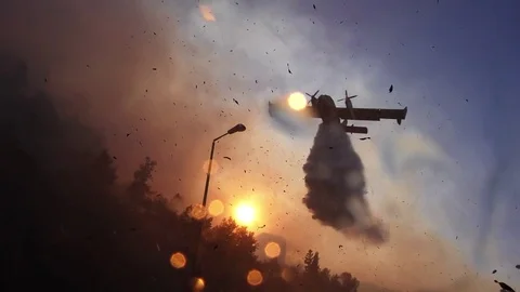 Amphibian airplane drops fire retardant on a forest near gas station. Stock Footage