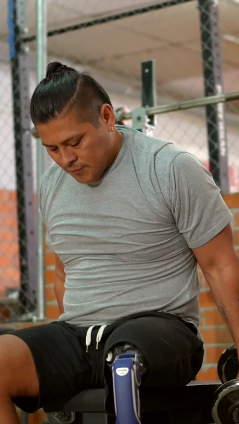 Amputee man with prosthetic leg training shoulders with dumbbells in the gym Stock Footage 317759761