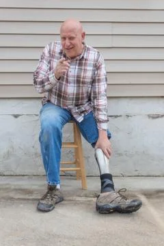 Amputee man on a stool looking forward pointing at the camera, reaching down Stock Photos