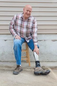 Amputee man on a stool looking forward reaching down to adjust prosthetic leg Stock Photos
