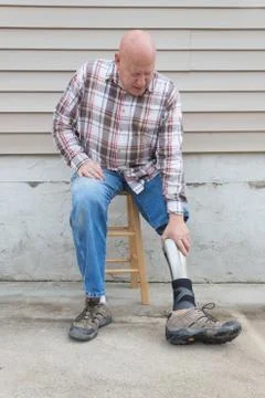 Amputee man on a stool reaching down to adjust prosthetic leg, copy space Stock Photos