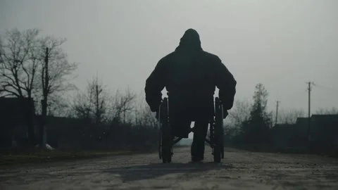 Amputee man in warm jacket rides wheelchair on ground road Stock Footage 154668799