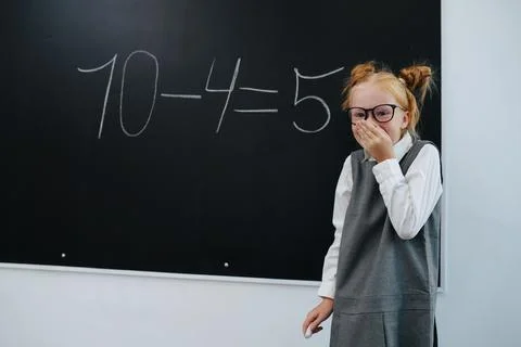 Amused giggling girl solving a basic math equasion on a blackboard in a class Stock Photos