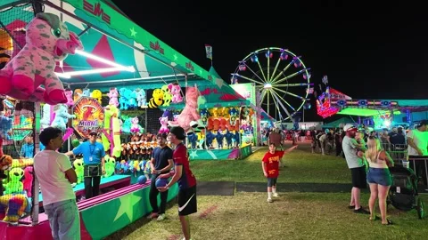 Amusement park game booth with a ferris wheel and crowd at night in Woodhaven Vídeo Stock 344021588