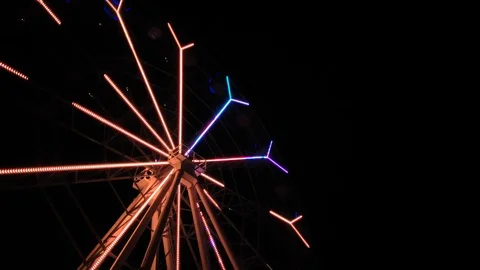 An amusement park. Multi coloured Ferris wheel rotates at night. Bright neon glo Stock Footage 106859663