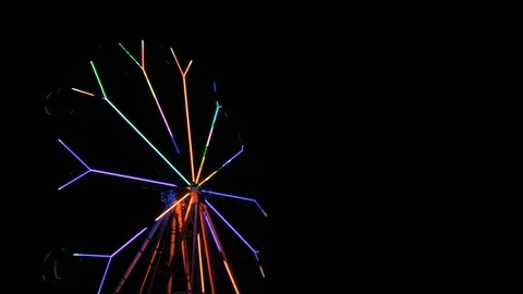 An amusement park. Multi coloured Ferris wheel rotates at night. Bright neon glo Stock Footage 106859697