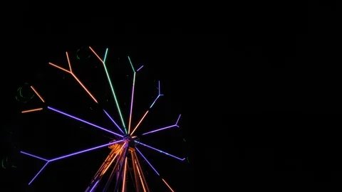 An amusement park. Multi coloured Ferris wheel rotates at night. Bright neon glo Stock Footage 106864965