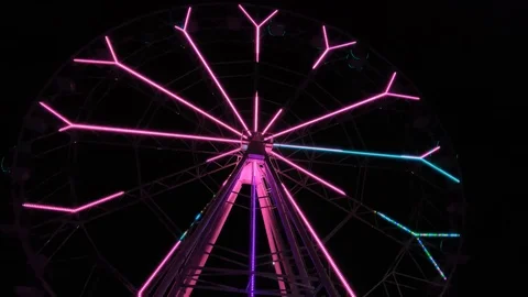 An amusement park. Multi coloured Ferris wheel rotates at night. Bright neon glo Stock Footage 106865268