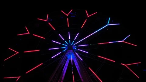 An amusement park. Multi coloured Ferris wheel rotates at night. Bright neon glo Stock Footage 106870288