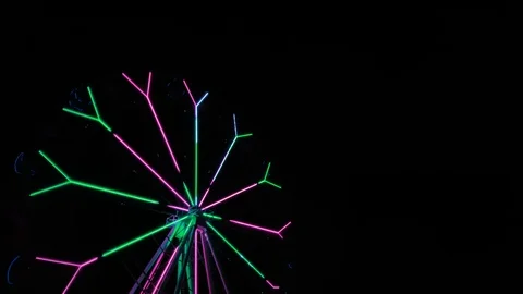 An amusement park. Multi coloured Ferris wheel rotates at night. Bright neon glo Stock Footage 106870615