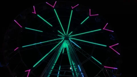 An amusement park. Multi coloured Ferris wheel rotates at night. Bright neon glo Stock Footage 106870641