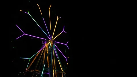 An amusement park. Multi coloured Ferris wheel rotates at night. Bright neon glo Stock Footage 106870663