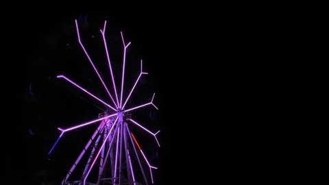 An amusement park. Multi coloured Ferris wheel rotates at night. Bright neon glo Stock Footage 106889403