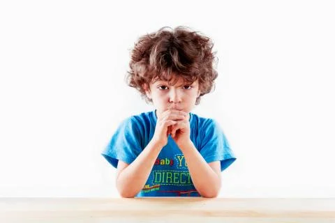 The amusing curly-headed kid bites hands and looks in the camera. On a gray b 스톡 사진
