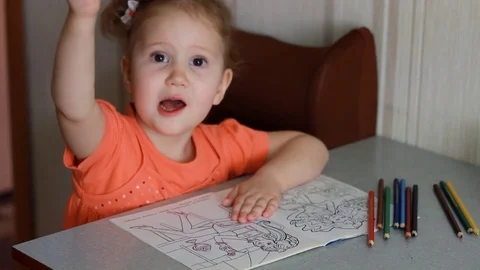 An amusing pretty girl sits at a table and draws in multicolored pencils. Child Stock Footage 81437720