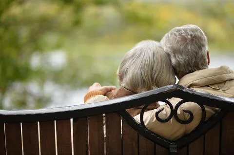 Amusing senior couple sitting on bench in park Stock Photos
