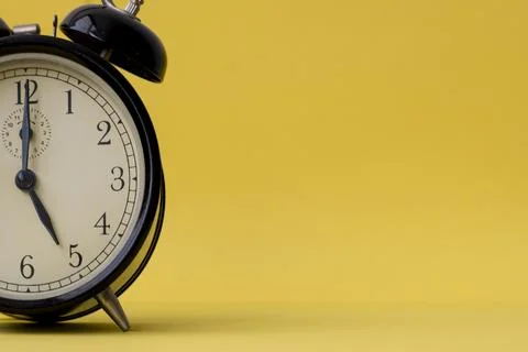 Analog alarm clock displaying five o'clock on a yellow background with copy.. Stock Photos