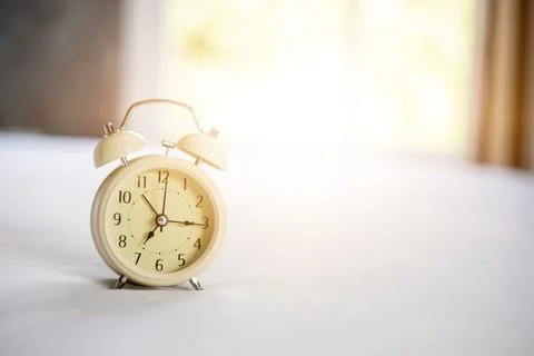 Analog alarm clock on white bed, time in the morning with a bright sunshine Stock Photos