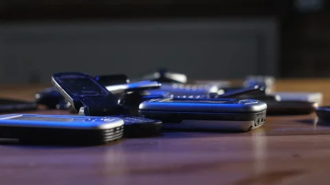 Analog communication. Old broken dusty cell phones lie on table in neon light. 動画素材 128095624