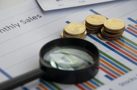 Analysis of data, chart and graphs with magnifying glass and gold coins backg Stock Photos
