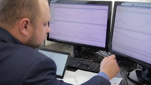 An analyst in suit builds schedule looking at two large monitors. Video stock 85277231