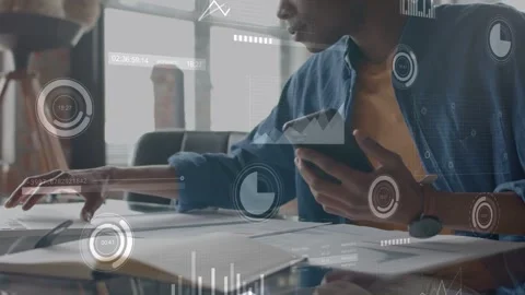 Analyst tapping phone at desk scanning charts while data overlays showing Stock Footage 333936527