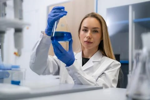 Analytical chemist examining blue liquid in Erlenmeyer flask within laboratory Stock Photos