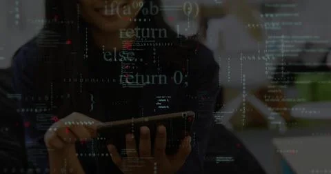 Analyzing code, developer wearing dark top using tablet at office desk, monitors Stock Photos