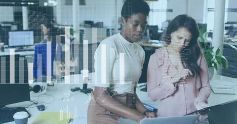 Analyzing data charts image over diverse businesswomen collaborating in office 写真素材