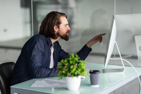 Analyzing data. Thoughtful young man trader is pointing at graphs on computer Stock Photos