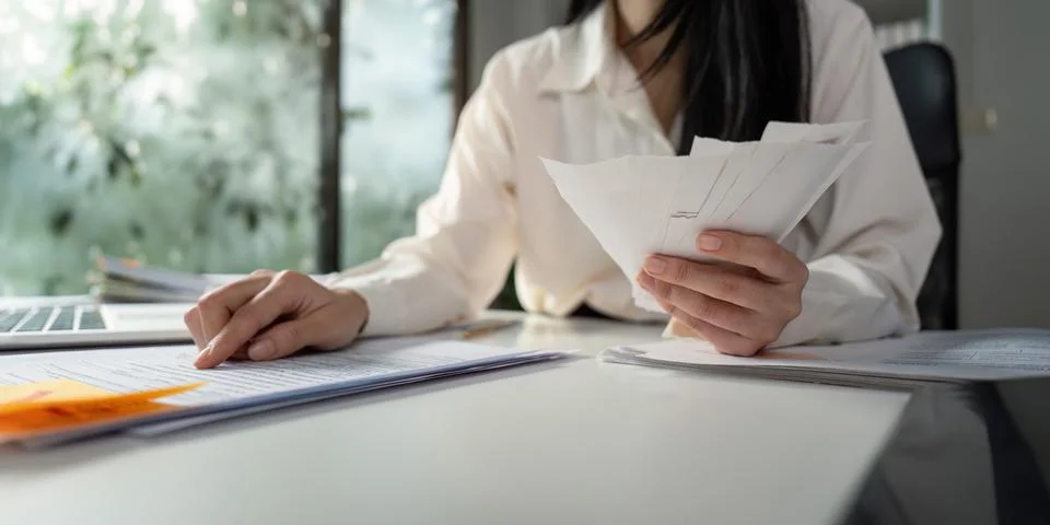 Analyzing financial data while sorting through tax paperwork at a desk. Stock Photos