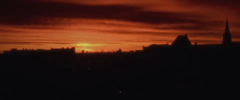 Anamorphic film shot of the sun setting behind silhouetted rooftops Stock Footage 302281009