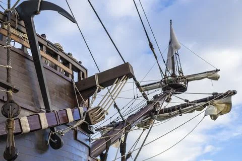 Anchor, masts and rigging of old pirate ship on background of cloudy blue sky Stock Photos