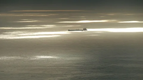 Anchored container ship with small boat on big light patches shimmering ocean 库存影片 88250985