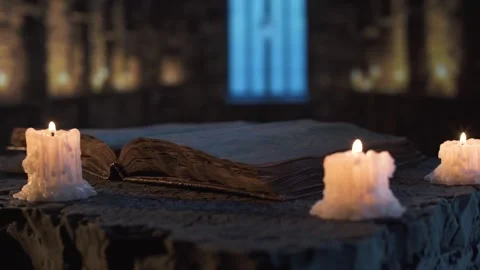 Ancient book with candles on a stone table in dim light in medieval stone room. Stock Footage 310336754