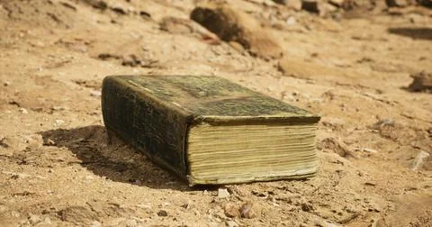 Ancient book resting on dry soil in an outdoor setting during daylight Stock Illustration