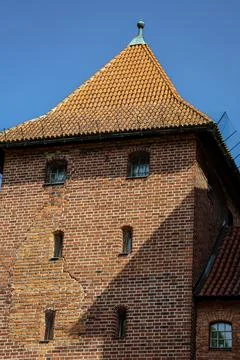 Ancient brick tower with a red tiled roof against a clear blue sky Stock Photos