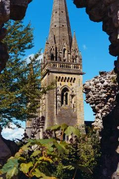 Ancient catholic cathedral tower in the frame of the ruins and green plants Stock Photos