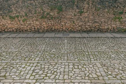 Ancient cobblestone pavement and rustic stone wall with patches of greenery Stock Photos