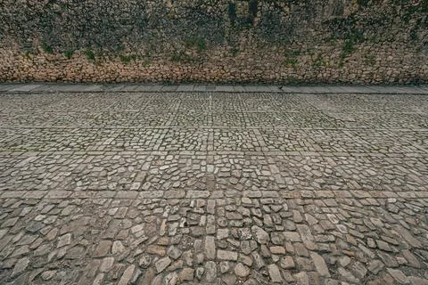 Ancient cobblestone pavement and rustic stone wall with patches of greenery Stock Photos