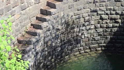 Ancient helical stepwell with spiral stone stairs transitioning into rippling wa 库存影片 337351768