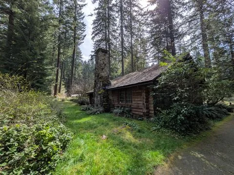 Ancient log cabin with moss-covered timber walls, stone chimney 库存照片