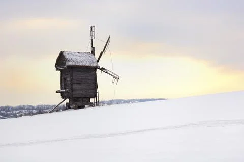 Ancient log windmill in a snow covered field lonely silhouette over sunset sky Foto stock