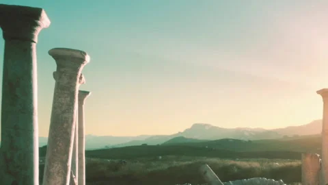 Ancient pillars stand against backdrop of hills at sunset in open field Stock Footage 339870338