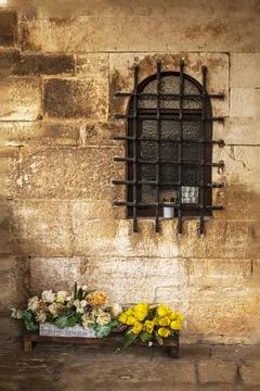 Ancient semicircular window with bars in a Roman masonry wall with flowers .. Stock Photos