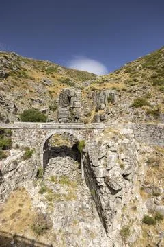 Ancient stone arch bridge spanning rugged mountain terrain Stock-Fotos