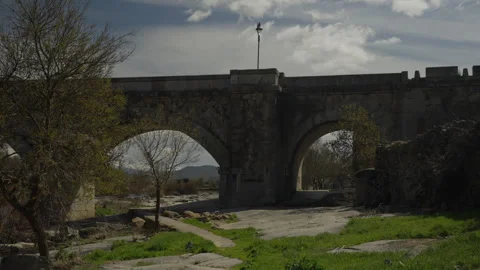 Ancient stone arched bridge crossing a vast dry riverbed with spring trees .. Stock Footage 335461253