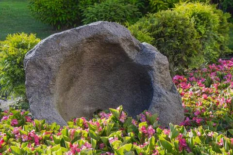 Ancient stone basin surrounded by pink flowers and green shrubs in a landsc.. Foto stock