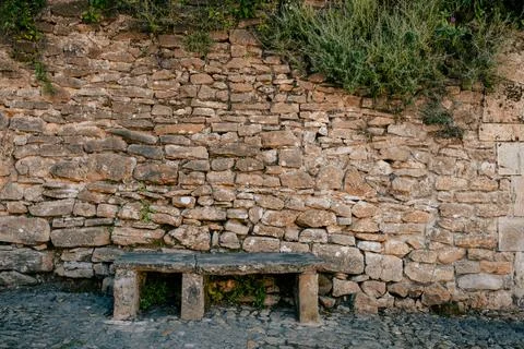 Ancient stone bench against rustic dry stone wall with vegetation Stock Photos
