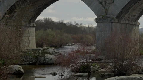 Ancient stone bridge arches crossing a calm river in rural Spain Stock Footage 335461531